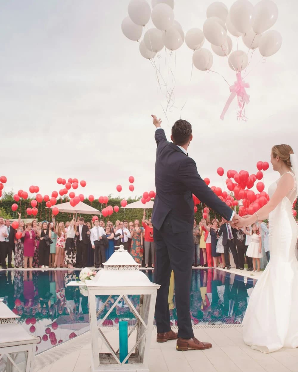 Bride and groom celebrating with guests and red balloons at an outdoor wedding reception