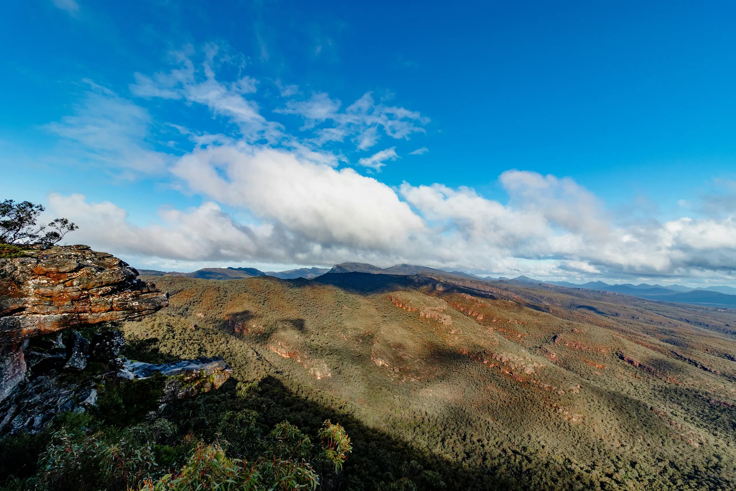 View from a sandstone clifftop across forested ridges and distant ranges in Grampians National Park